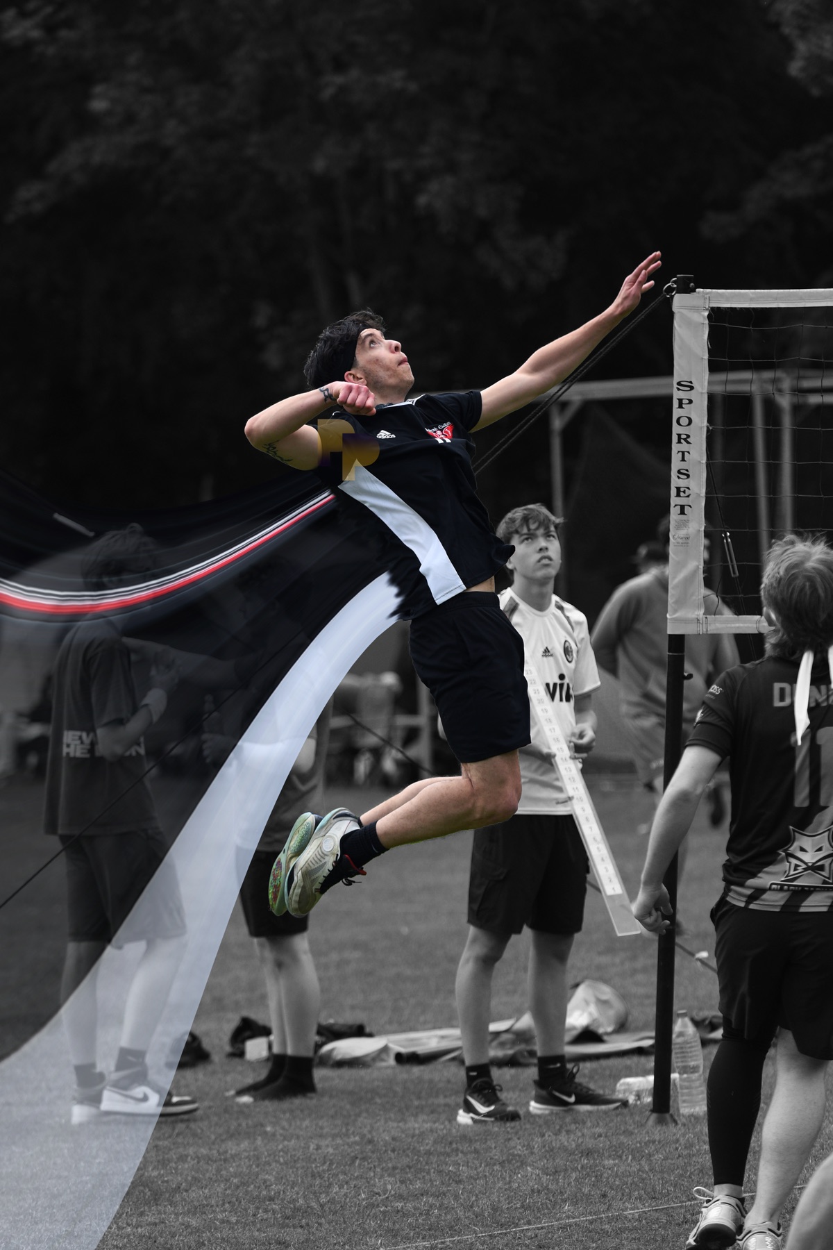 A player arches for an outdoor spike on grass, a monochrome ribbon sweeping past